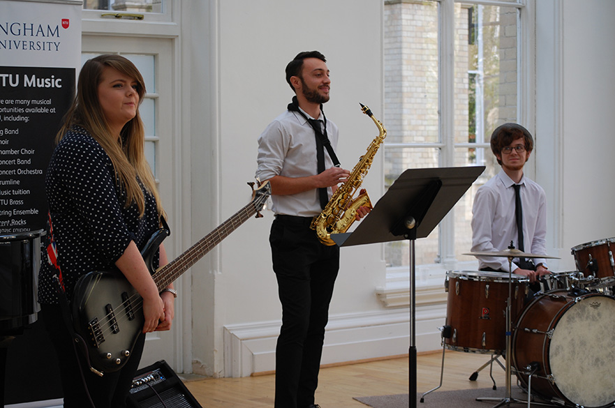 A female bassist, male saxophonist and male drummer.