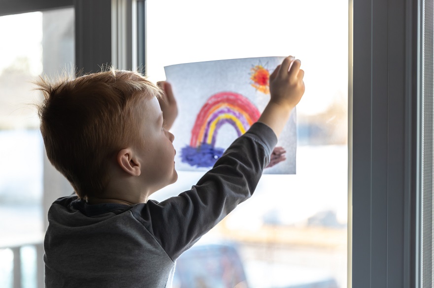 Child putting a rainbow picture on the window