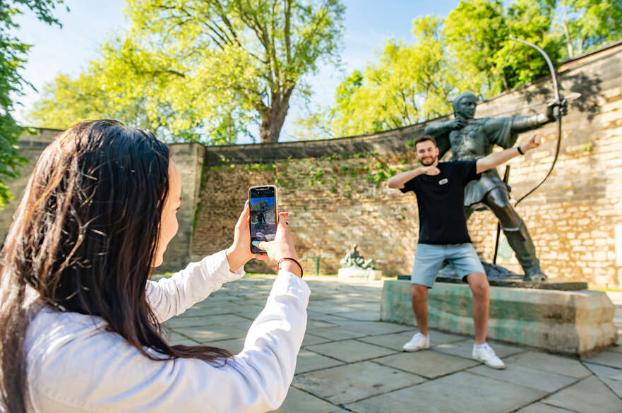 A student having his picture taken by a friend, posing in front of the Robin Hood statue.