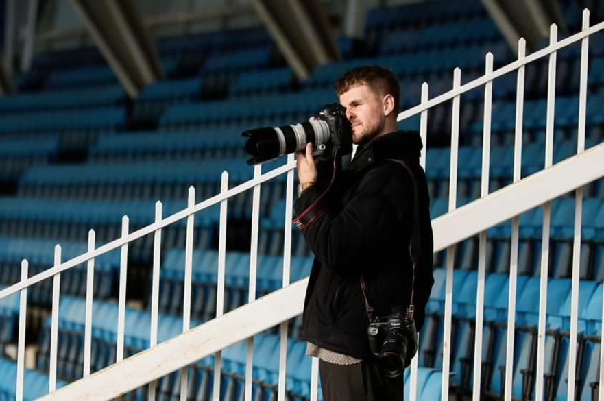 Student in a football stadium seating area taking pictures with a sports camera