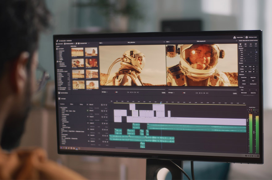 A person sits at a desk editing video in Adobe Premiere Pro, with a monitor showing a colour-graded astronaut scene, multiple timeline tracks, and audio levels on screen.