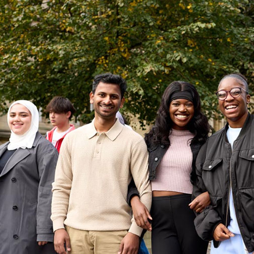 Four students standing on campus and smiling.