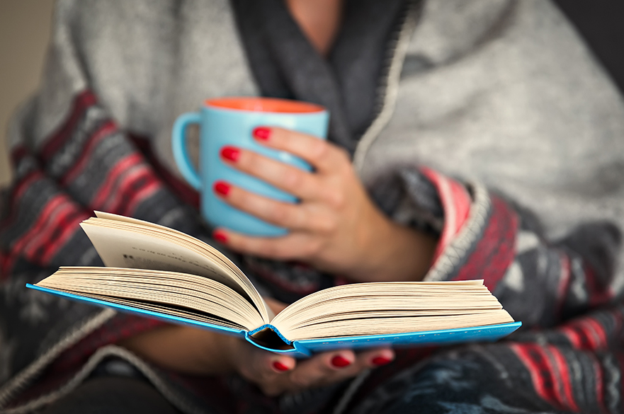 A girl holding a book and a mug of tea.