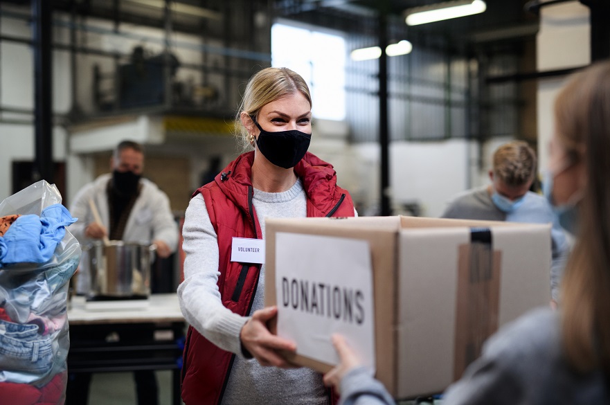 Women in a donation centre handing over a box while wearing a mask