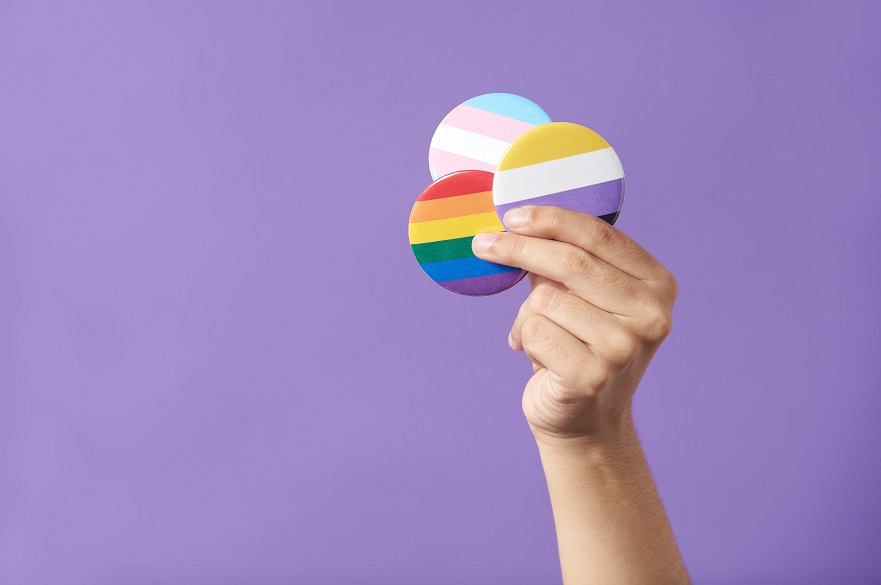 Hand raising three pins with rainbow, trans and non binary flags