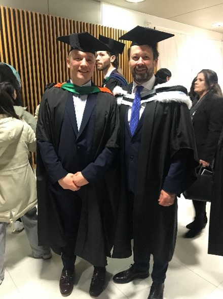 Student George and NTU academic Keith Lown posing for a photograph wearing their graduation gowns.