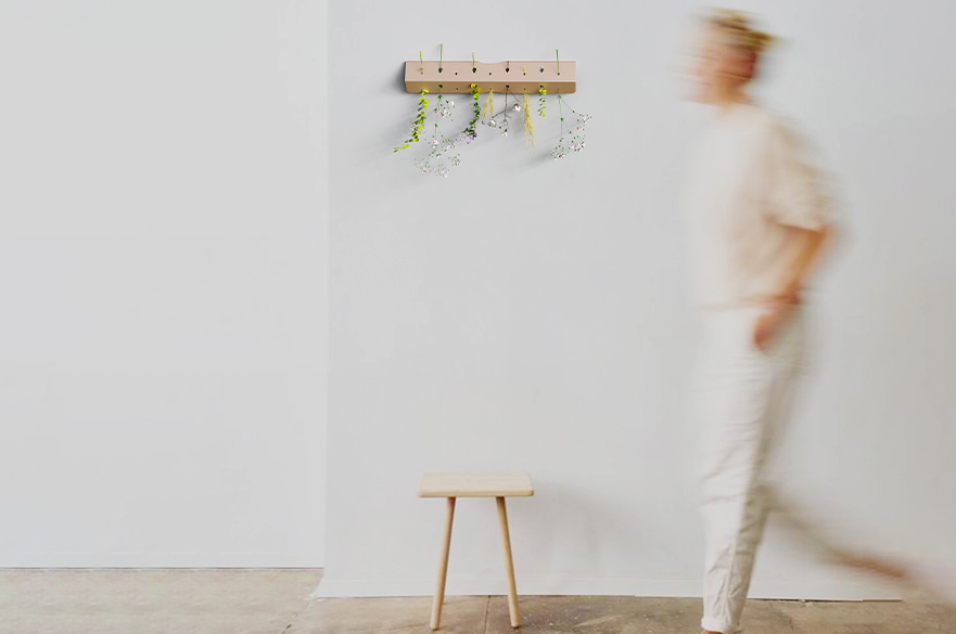 Person walking past a wooden stool and a wooden clothes hanger with flowers dangling from it.