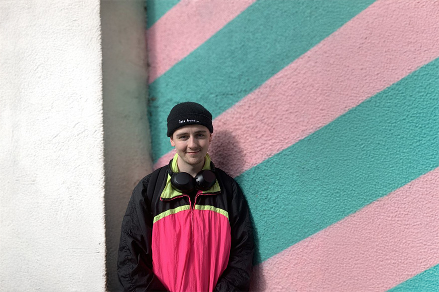 Phillip smiling and standing next to the a colourful wall