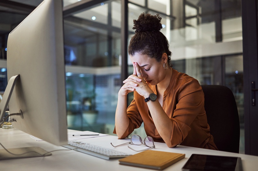 Woman sitting at her desk with her head in her hands, sign of trauma in the workplace
