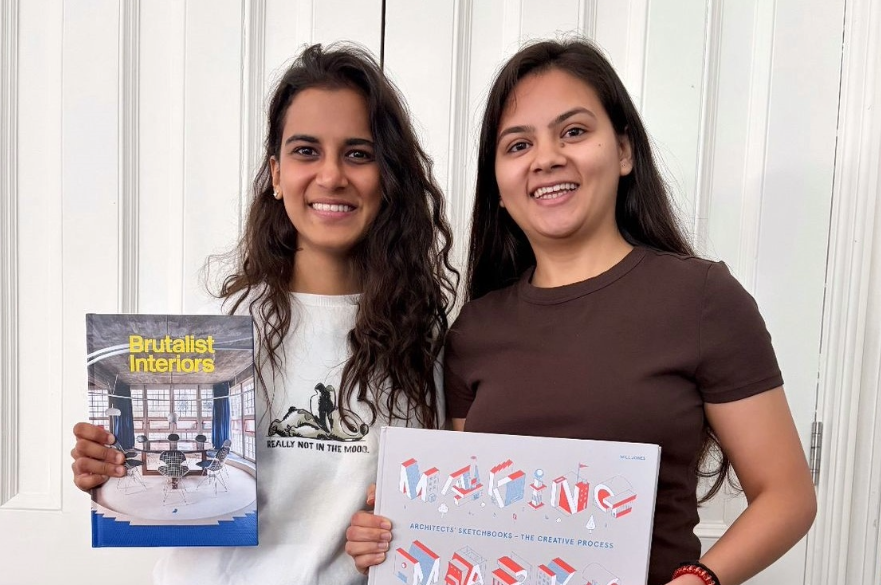 Two students posing for a photo. They are both holding books about architecture.