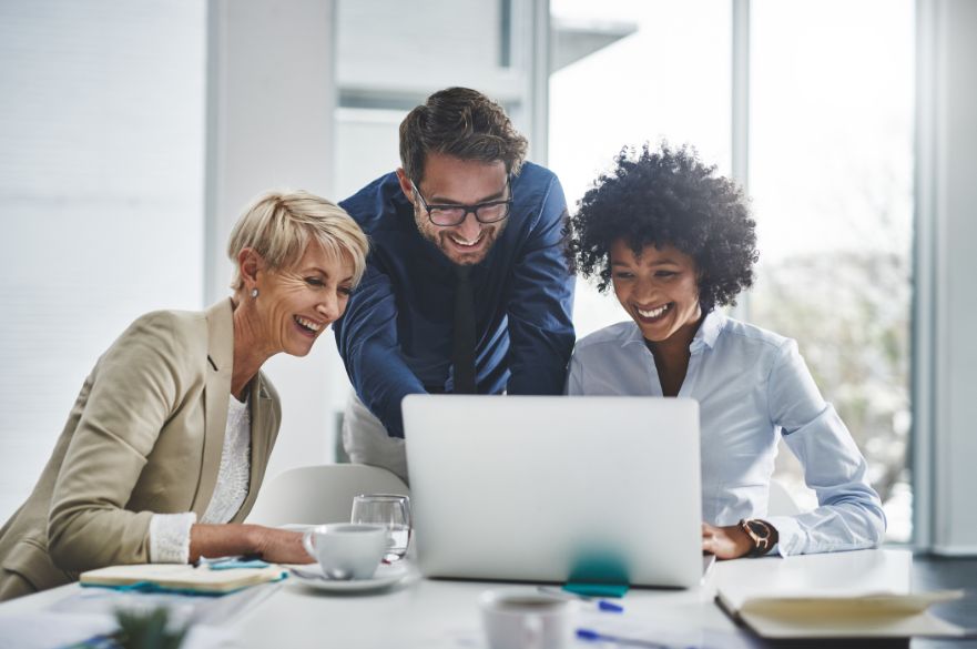 Three workers around a computer smiling
