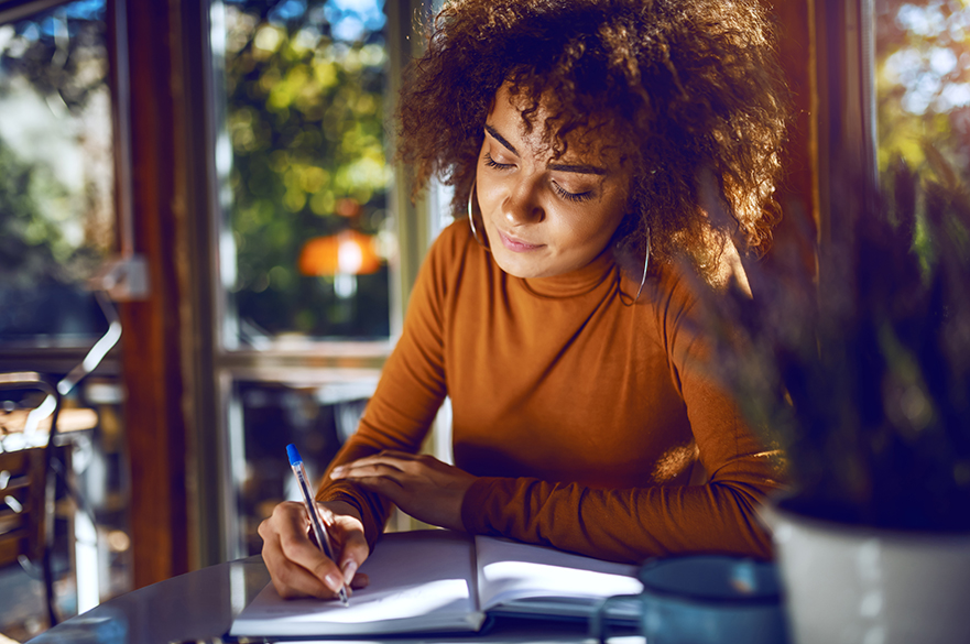 Girl sat at a table writing in a notebook.
