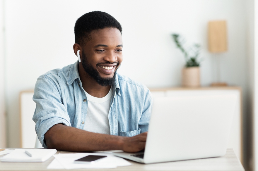 Man sat at table smiling at laptop