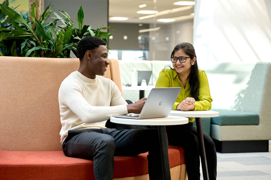 Two students chatting and laughing while they look at a laptop in NTU's Postgraduate Centre