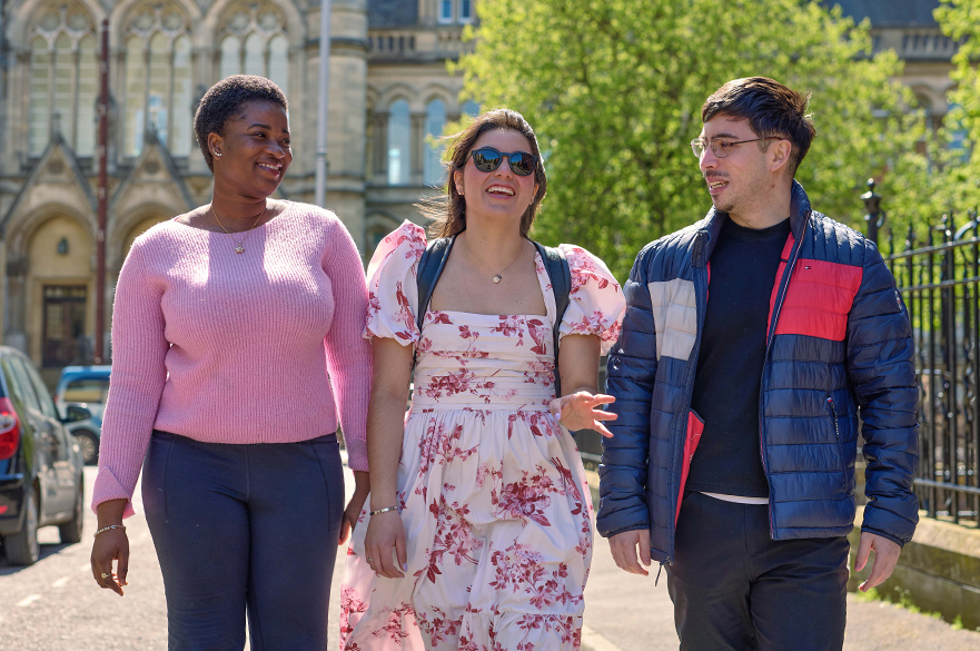 Three students walk towards camera with Arkwright building in the background