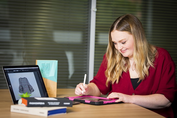 A woman in a red top sits at a desk with an ipad and stylo in hand