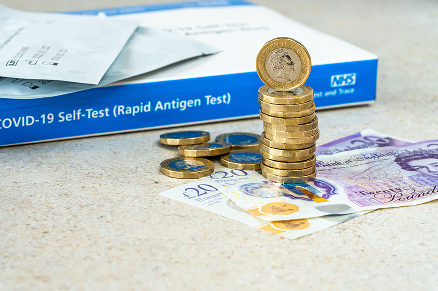 Covid test box in the background with pounds and twenty pound notes next to it