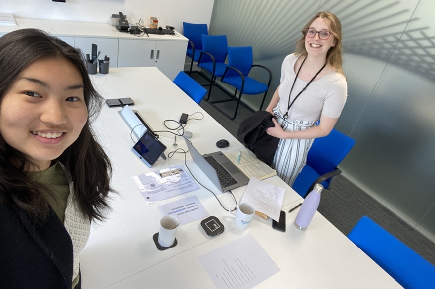 Two people stood either side of a desk, both smiling at the camera.