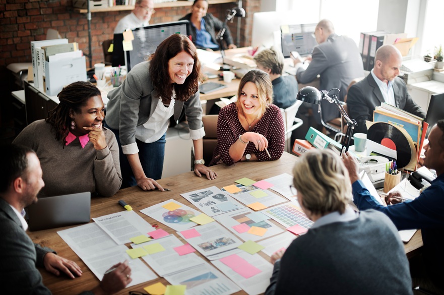Workers around a table in an office with smiling women stood up by them