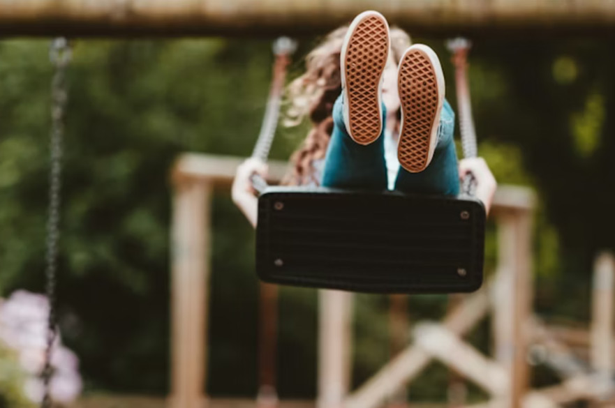 A child mid-swing on a swing, with the bottom of her shoes facing the camera.