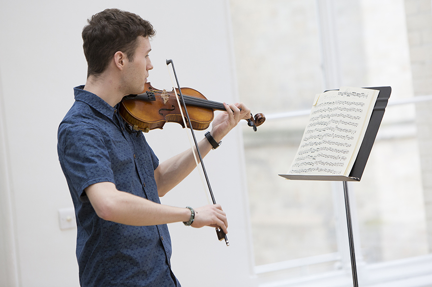 A male student playing the violin in front of a music stand.
