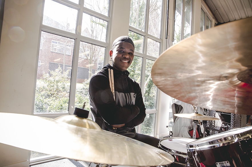 A male student sat at a drumkit.