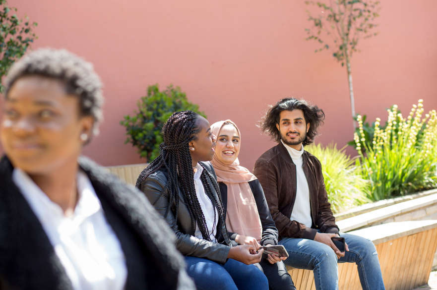 Three students having a conversation, smiling in the sun in the rooftop garden.