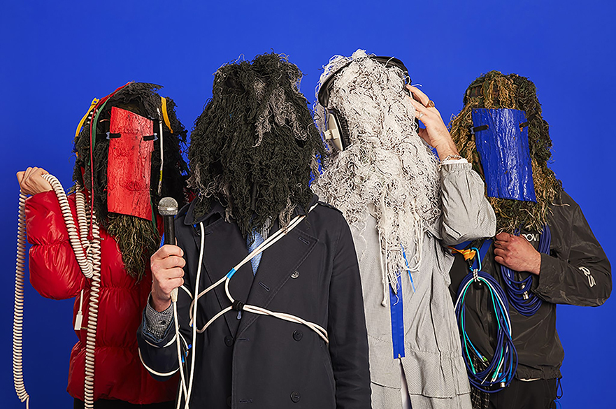 Snapped Ankles. Four people stand in a row with mops on their heads and concealing their faces.
