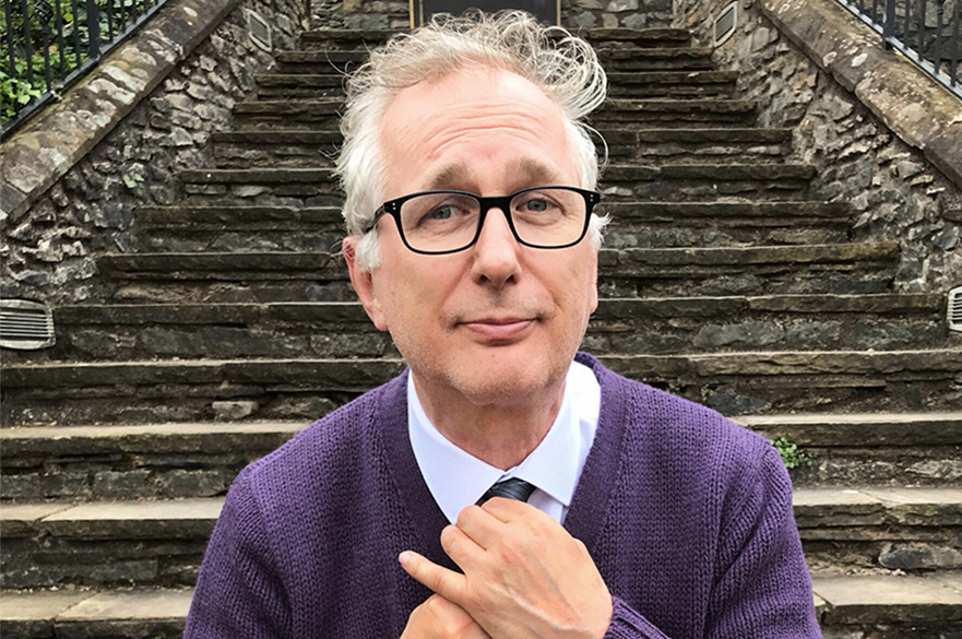 A man with grey hair and classes sat down on steps outdoors, fixing his tie.