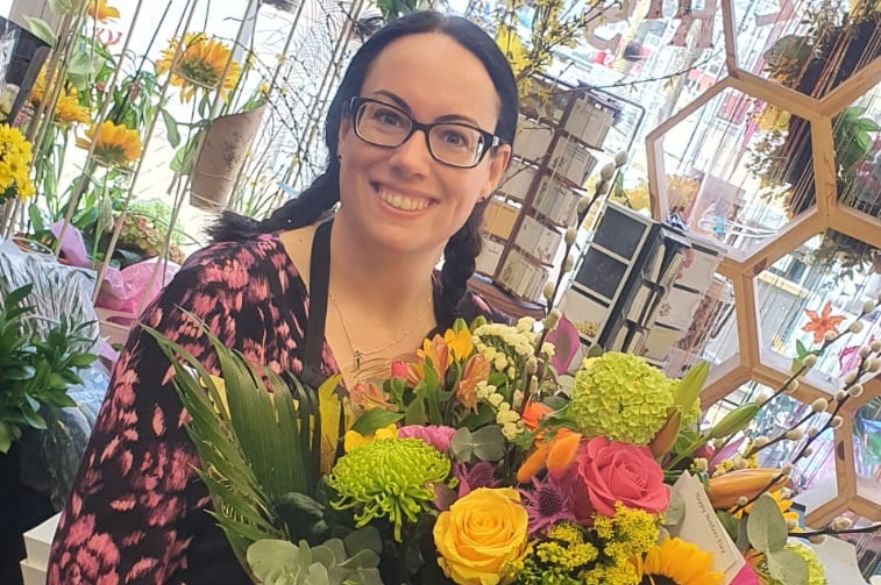 A lady stands in a florist holding a large bouquet of colourful flowers