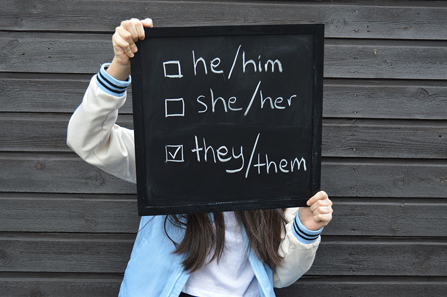 Teenager holding up chalkboard sign with different pronouns on