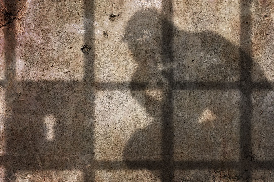 Shadow on a wall of a man sitting down behind prison bars