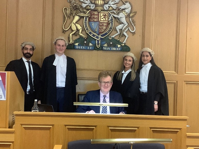 Four people in mooting outfit and a judge in a mooting court.