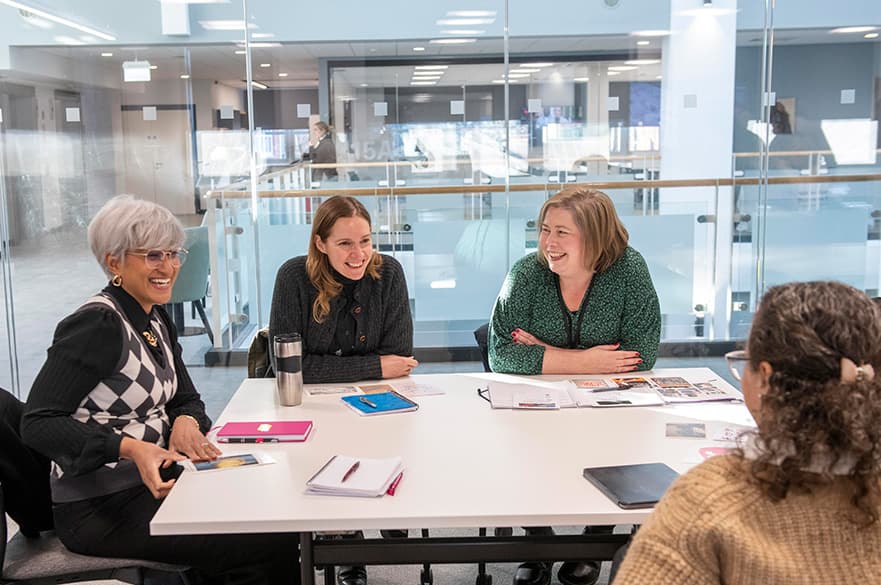 A group of mature students sitting around a table smiling at each other.