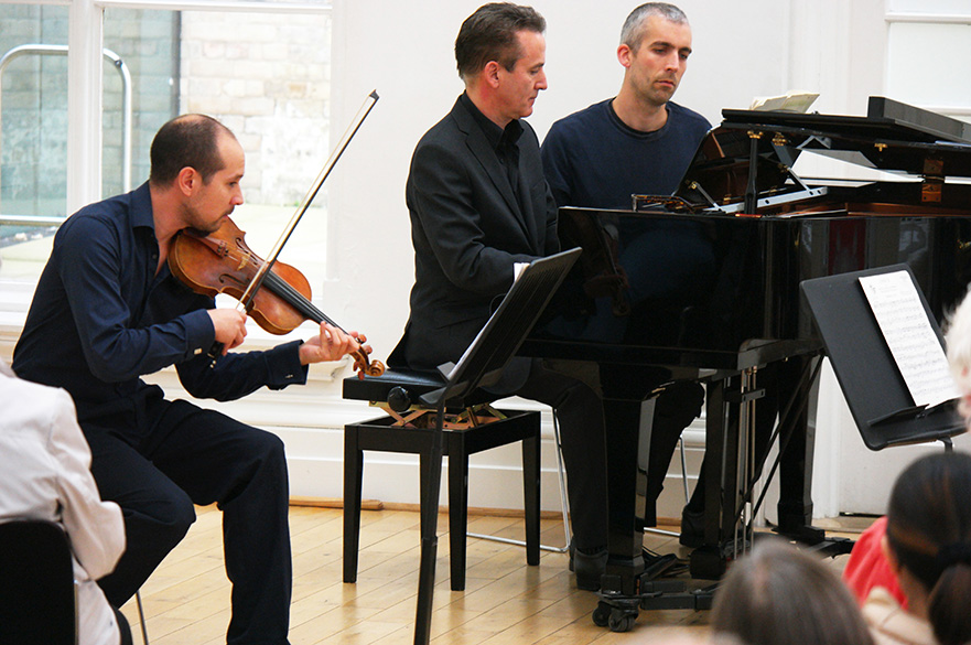 A male violinist and pianist playing in front of an audience.