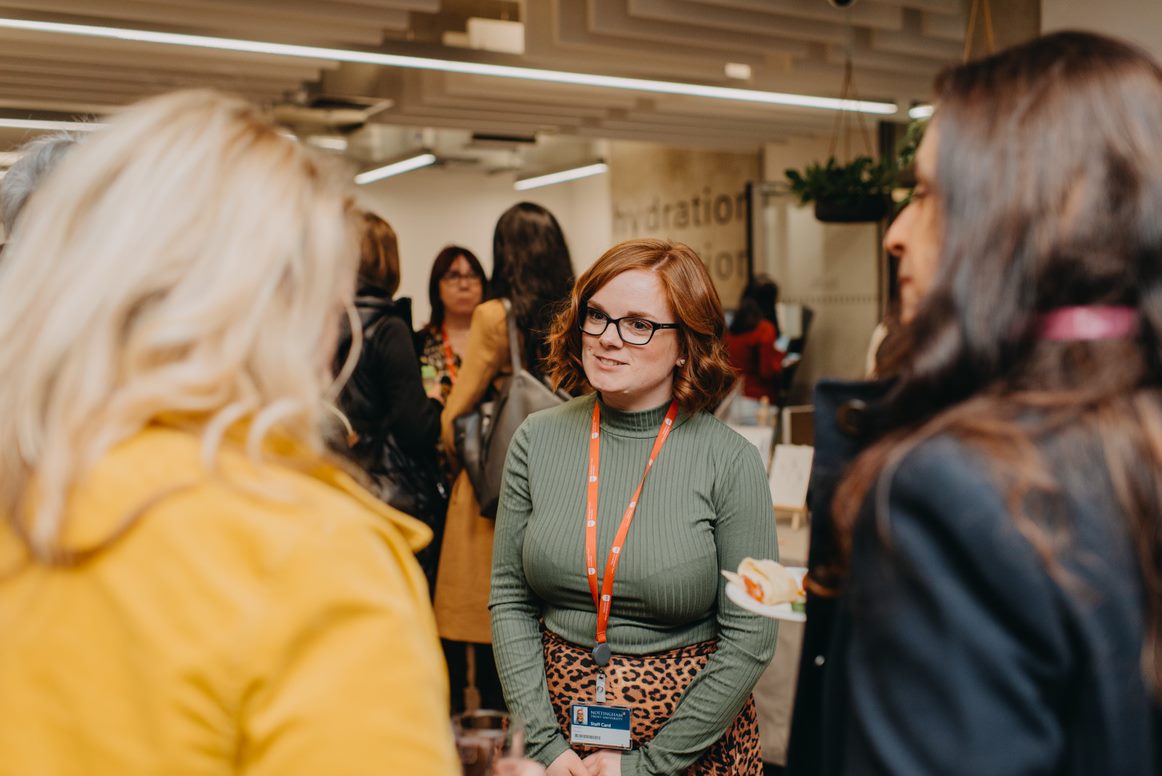 Ginger woman standing between other women smiling and talking (probably) about the business 