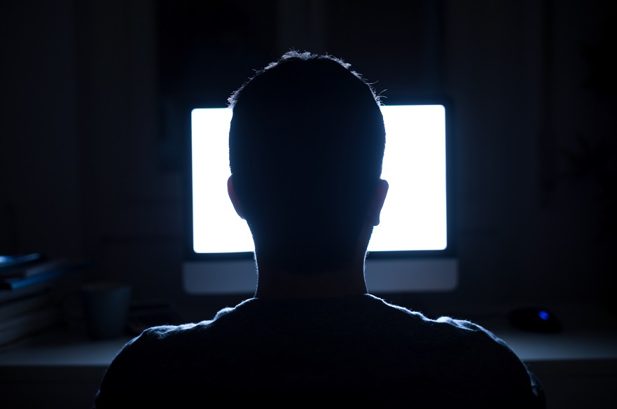 Silhouette of back of a man in the dark looking at computer screen
