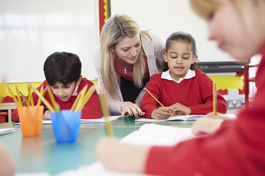 School teacher helping young children in a classroom to write