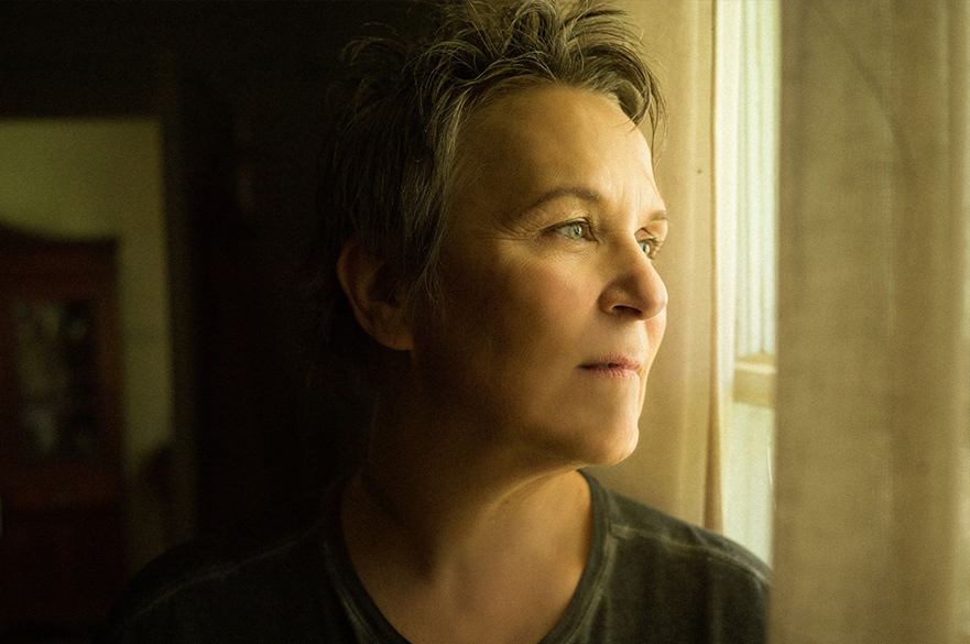 Photograph of Mary Gauthier looking out of a window with soft lighting.