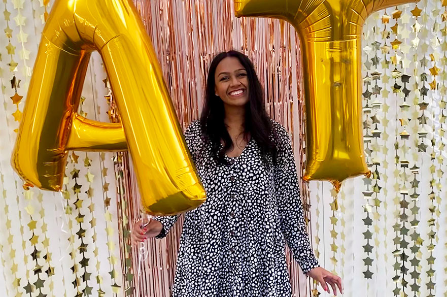 Raksha smiling at the camera holding two large golden baloons