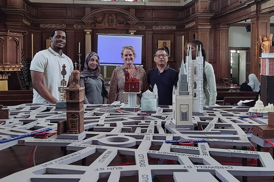 A group of four people standing in front of a table in a church. On the table is a 3D map of the London Underground system.