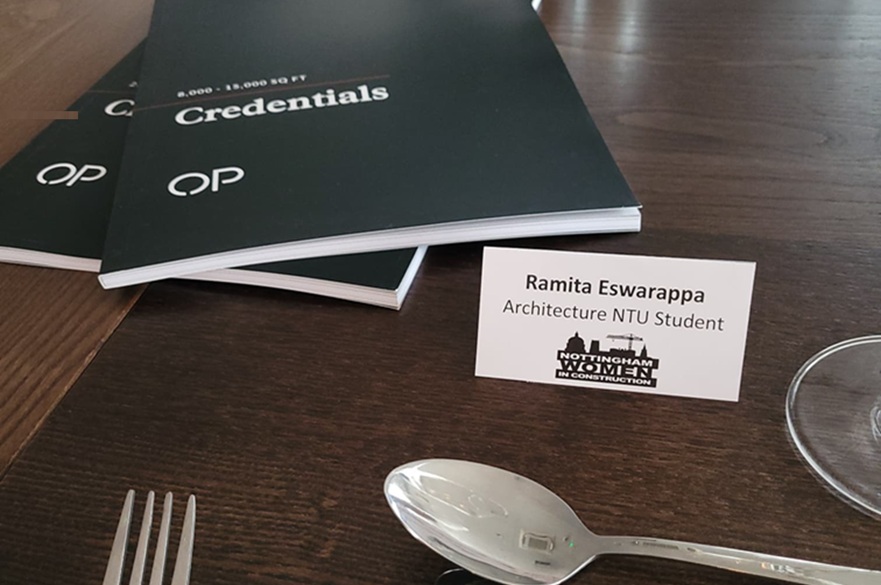 A name card on a table next to some pens, cutlery and branded stationery.