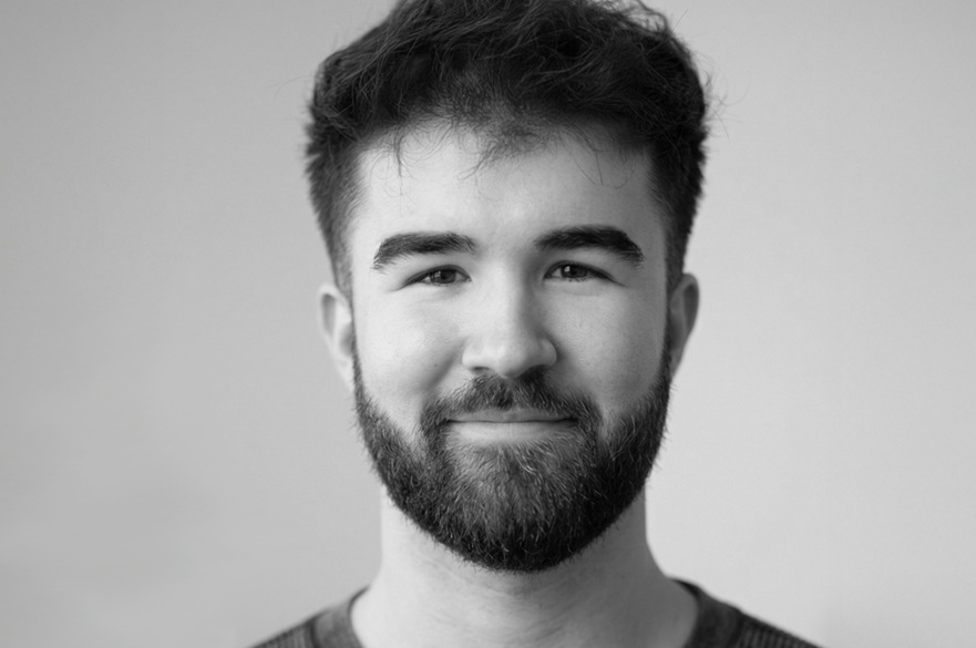 A black and white photo of a person smiling facing the camera.