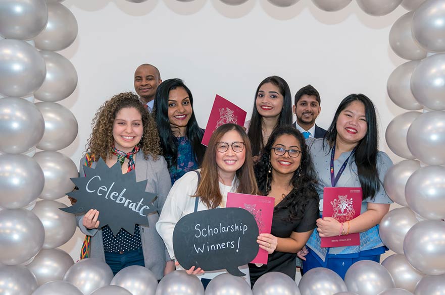 Smiling scholarship award winning students surrounded by an arch of silver balloons.