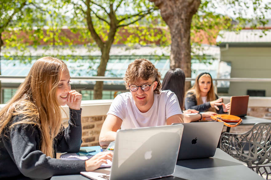 Two students sat working on Macbooks outside on the terrace.