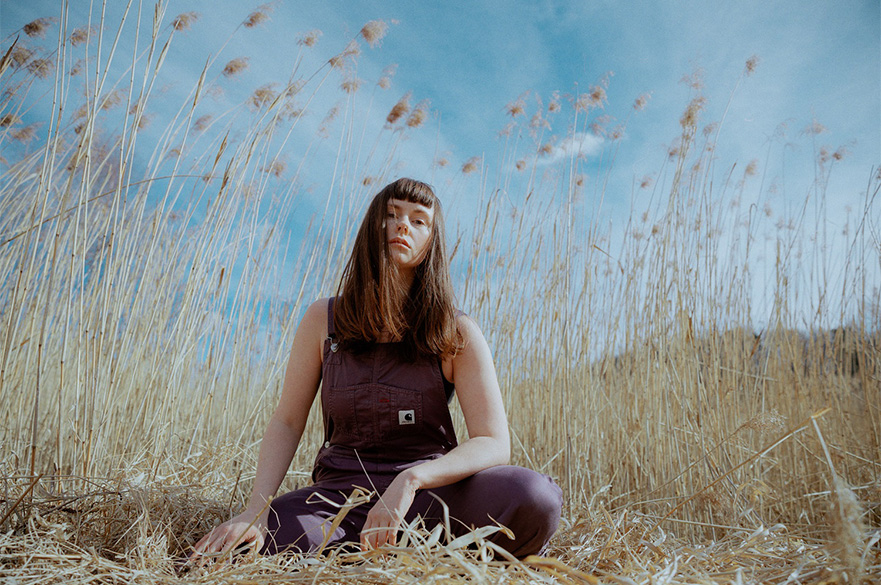 A woman with brown hair sat on the floor in a wheatfield 