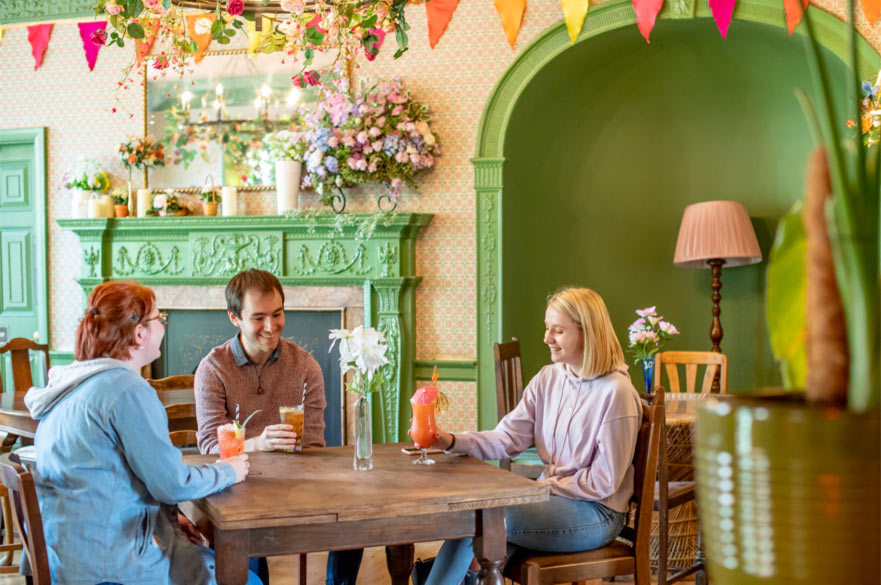 Three students having cocktails in an extravagant-looking bar decorated in green and pink.