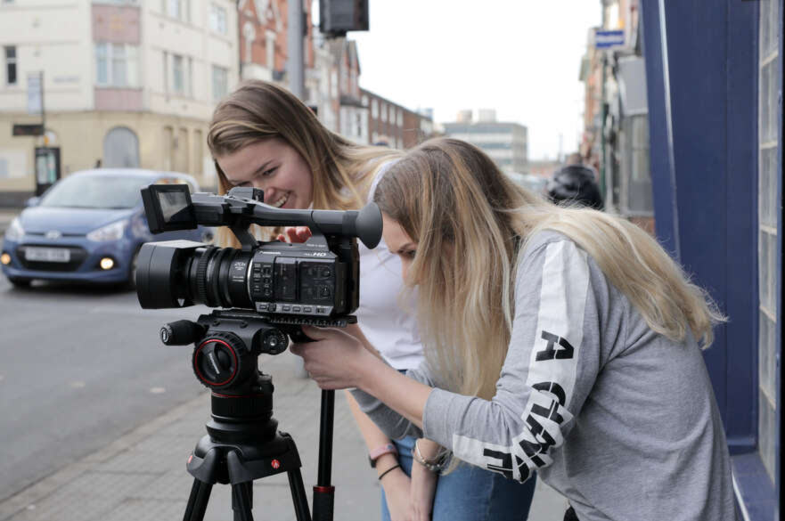 Two female students setting up a video camera on a tripod on a Nottingham street.