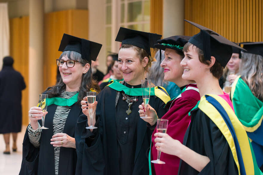 Four mature students in their graduation gowns, smiling and holding prosecco flutes.
