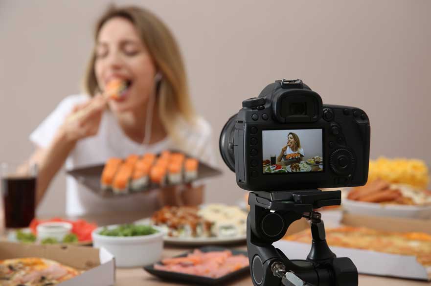 Female eating in front of a camera with lots of food on the table